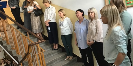 Powiększ grafikę: Nauczyciele ustawieni na schodach patrzą na gromadzących się na korytarzu uczniów