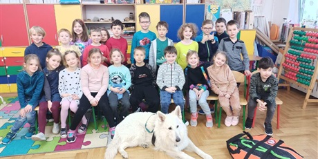 Powiększ grafikę: Grupka dzieci z psem ratownikiem w sali lekcyjnej na tle szafek szkolnych