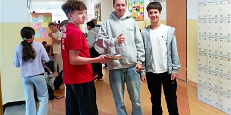 Powiększ grafikę: Na szkolnym korytarzu uczeń koła PP HOPR z tacą z orzechami, obok dwaj uczniowie częstujący się orzechami. W tle szafki szkolne i inni uczniowie