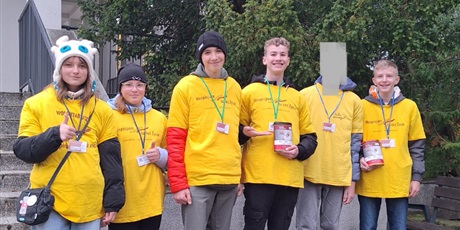 Powiększ grafikę: Sześcioro wolontariuszy stoi obok siebie. Ubrani są w koszulki wolontariuszy, na szyi mają identyfikatory. Dwóch chłopców trzyma w ręku skarbonki, a dwie dziewczynki pokazują kciuki do góry.