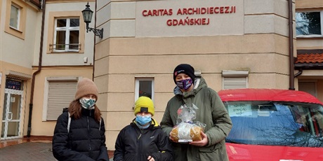 Powiększ grafikę: Wolontariusze stoją przed siedzibą Caritas w Sopocie i trzymają w ręku torbę pełną prezentów dla Chorych.